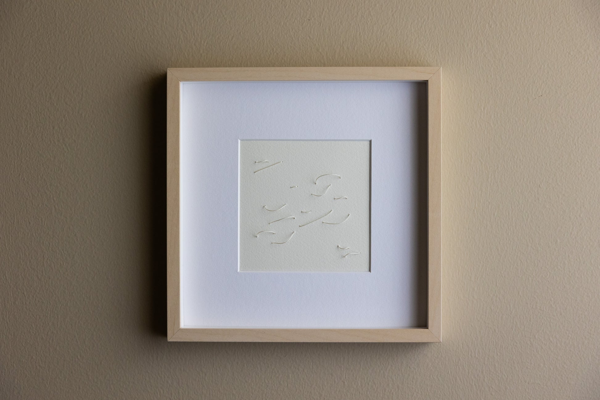 Framed abstract embroidery on paper, an original minimalist relief artwork representing white birds, changing with the light, soft light.